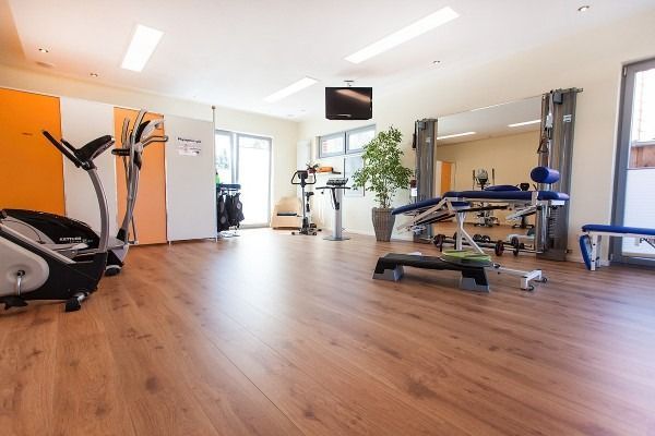Fitnessstudio-Interieur mit Trainingsgeräten: Laufband, Gewichte, Therapieliege und Stepper. 
