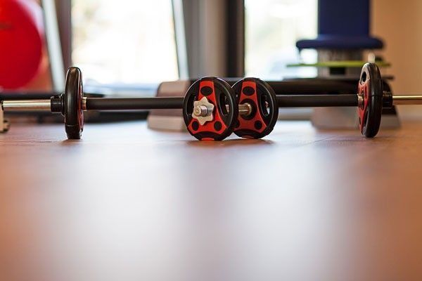 Ein modernes Fitnessstudio mit Holzboden, verschiedenen Trainingsgeräten, Bänken und einem kleinen Fernseher.