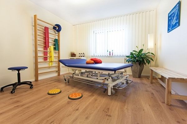 Physiotherapieraum mit Behandlungsliege, Trainingsgeräten und Holzboden.