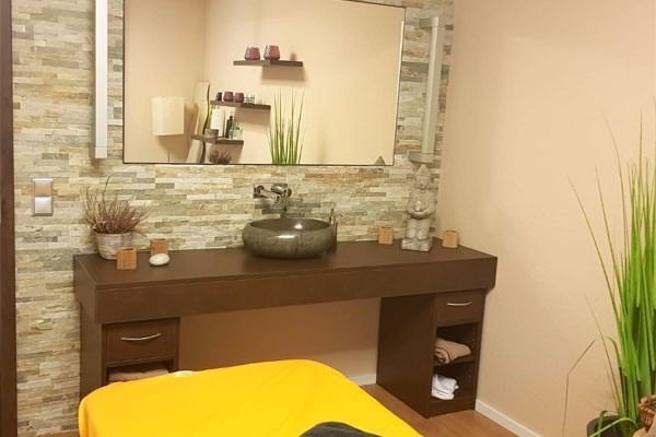 Spa-Interieur mit Massageliege, Waschbecken und Dekorationselementen.