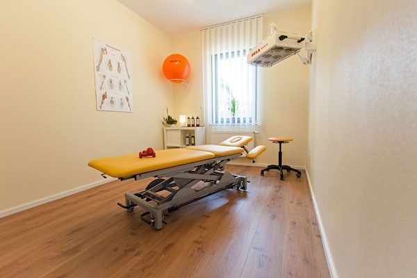 Physiotherapieraum mit gelber Behandlungsliege, orangefarbenem Gymnastikball und Fenster.