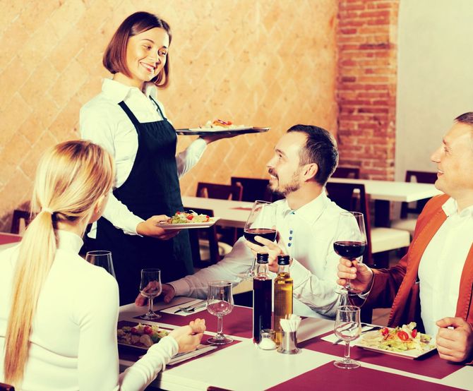 Una camarera está sirviendo comida a un grupo de personas en un restaurante.