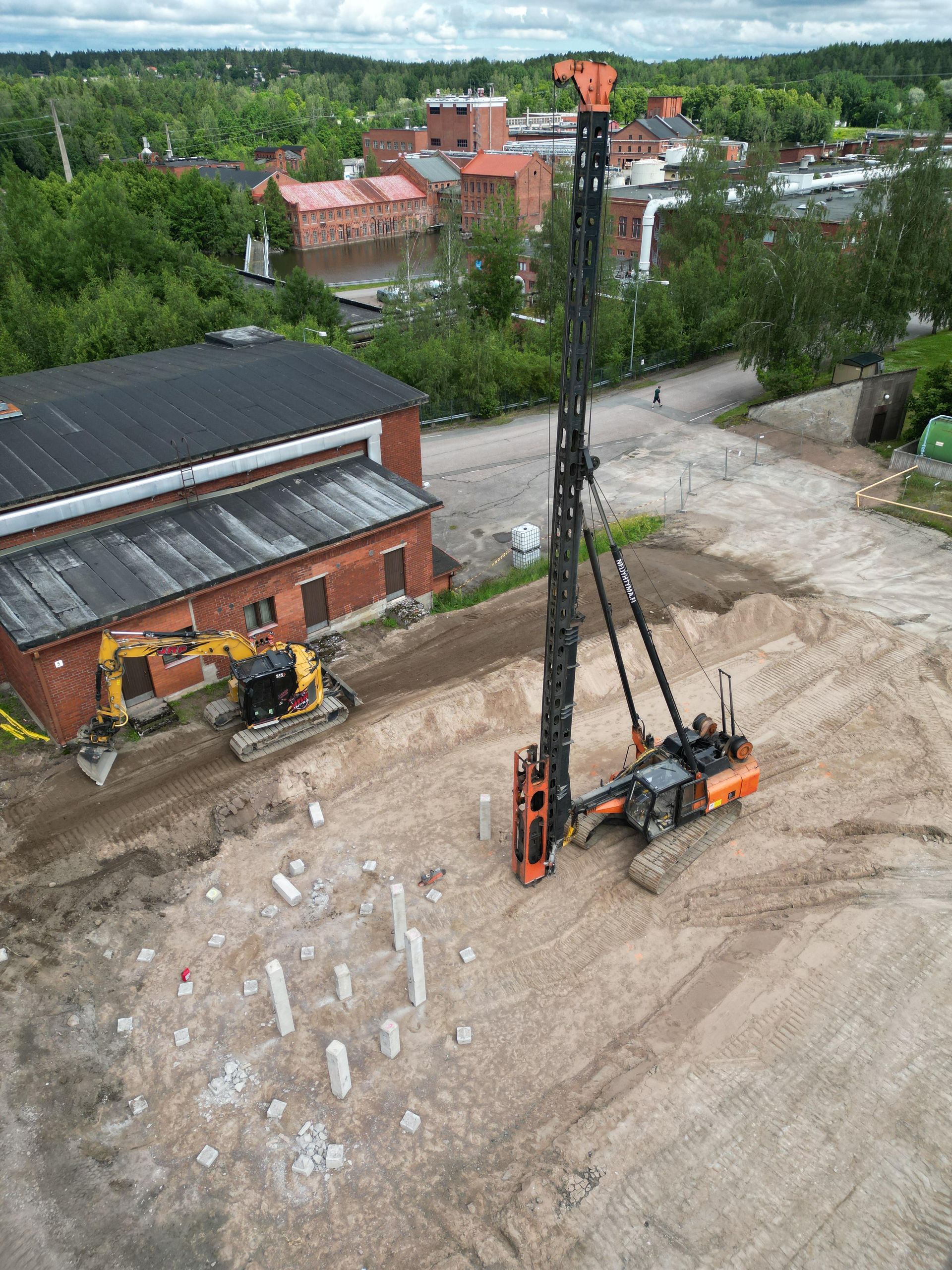 Rakennustyömaa, jolla on suuri porauslautta punatiilirakennuksen ja soratontin vieressä.