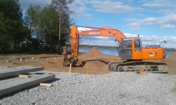 Oranssi kaivinkone kaivaa maakasaa rakennustyömaalla sinisen taivaan alla.