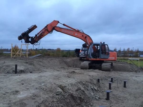 Oranssi kaivinkone työskentelee mutaisella rakennustyömaalla pilvisen taivaan alla.