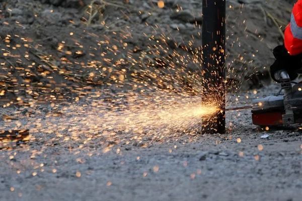 Henkilö käyttää hiomakonetta metallipylvään päällä ja lähettää kirkkaita kipinöitä karhealle ulkopinnalle