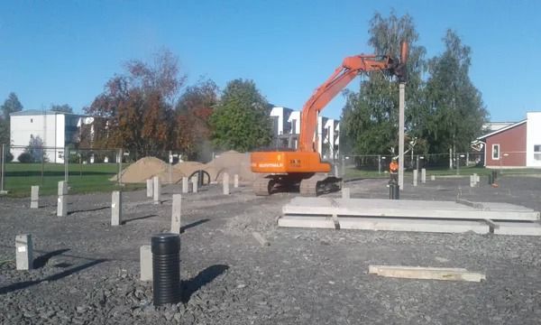 Oranssi kaivinkone soratyömaalla, taustalla betoniaidat ja puut