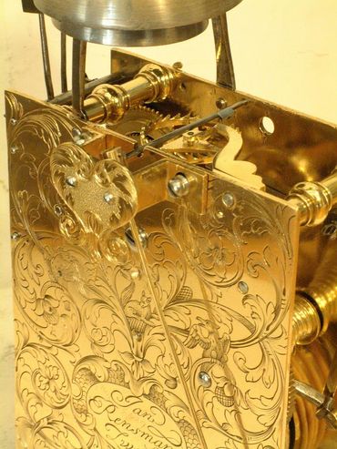 Dispositif mécanique orné, plaqué or, avec des motifs floraux gravés et des engrenages visibles sous une lampe.