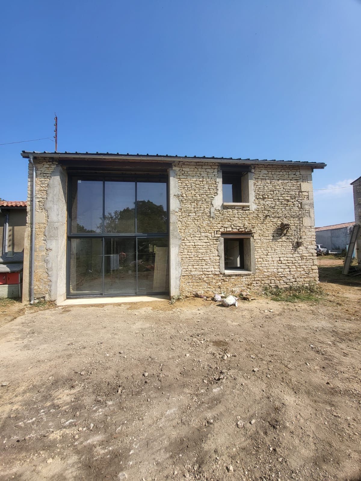 Bâtiment en pierre avec de grandes portes vitrées, deux petites fenêtres et un ciel bleu clair.