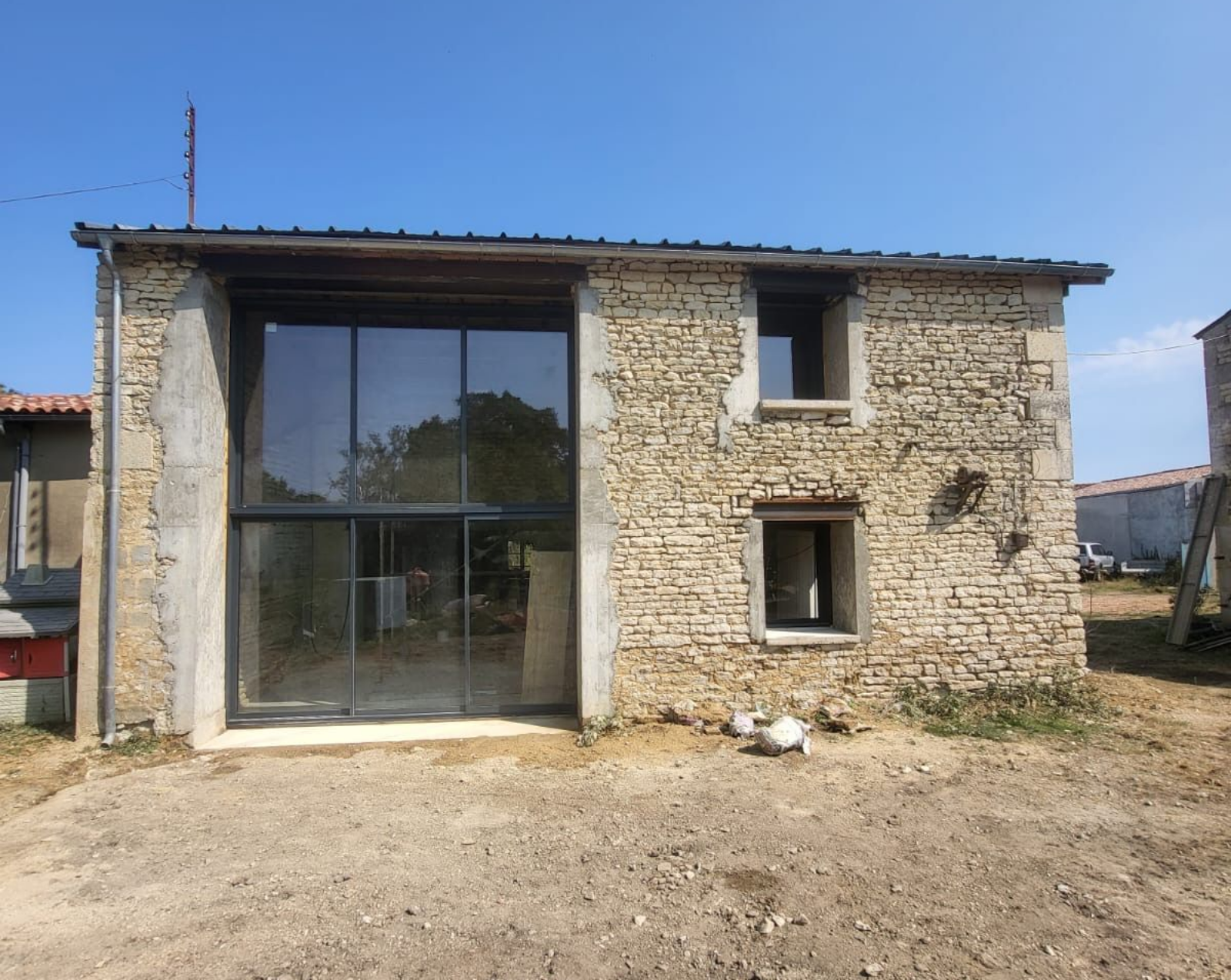 Bâtiment en pierre avec de grandes portes vitrées. Deux fenêtres à droite. Ciel bleu.