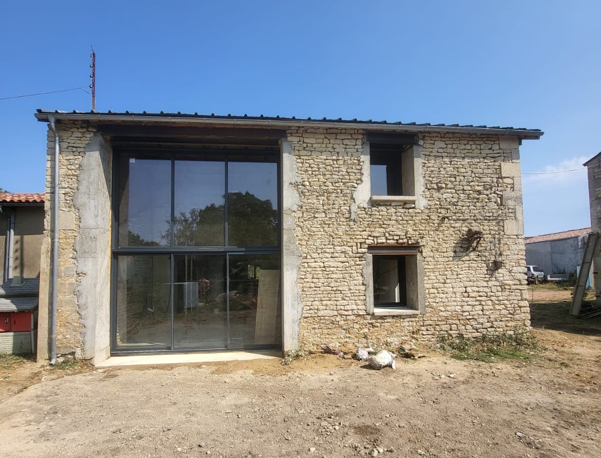 Bâtiment en pierre avec de grandes portes vitrées et de petites fenêtres sous un ciel bleu clair.