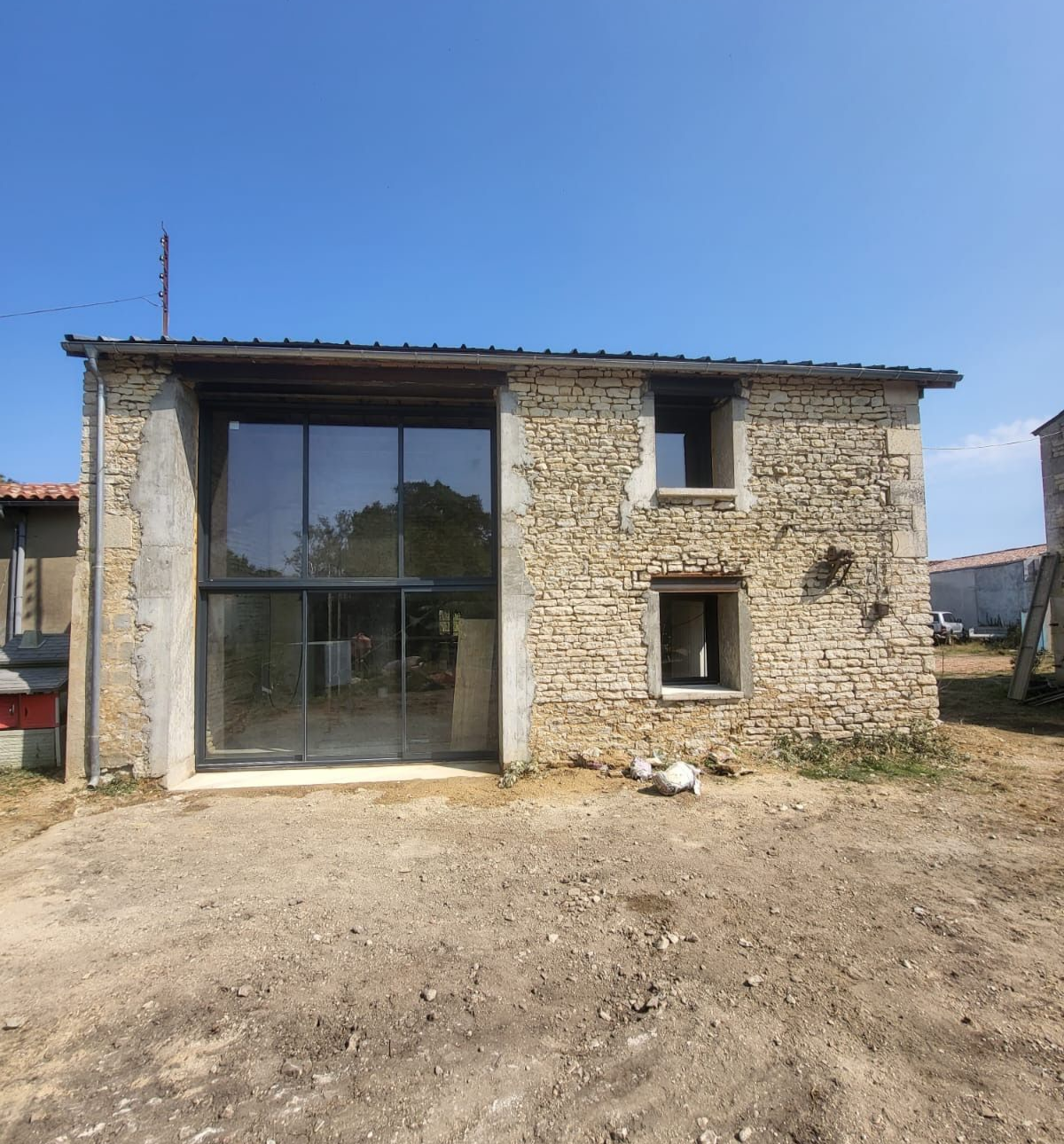 Bâtiment en pierre avec de grandes portes vitrées et deux petites fenêtres, sous un ciel bleu limpide.