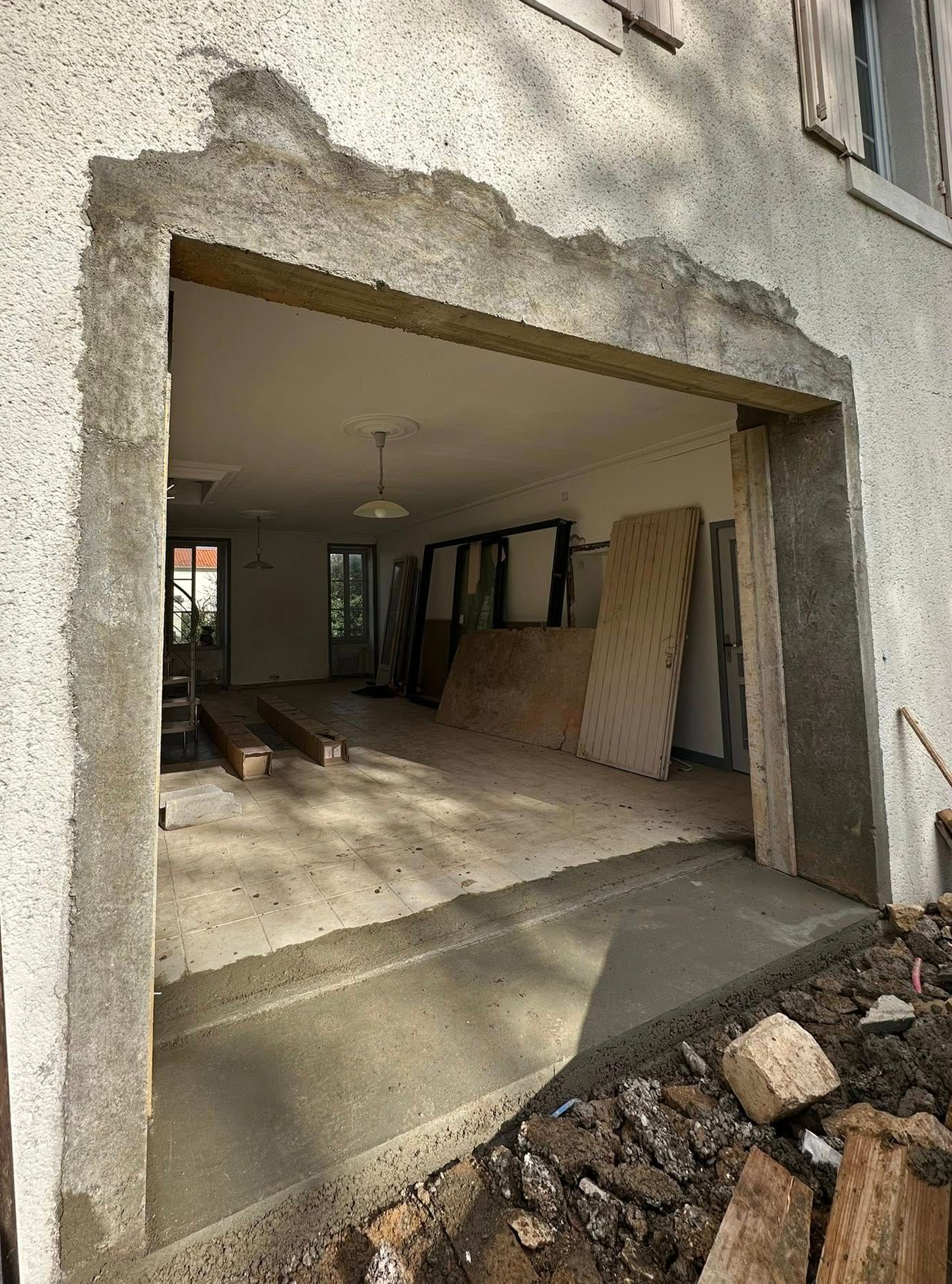 Vue extérieure d'une ouverture de bâtiment avec ossature apparente. Intérieur visible : pièce, matériaux et allée en béton.