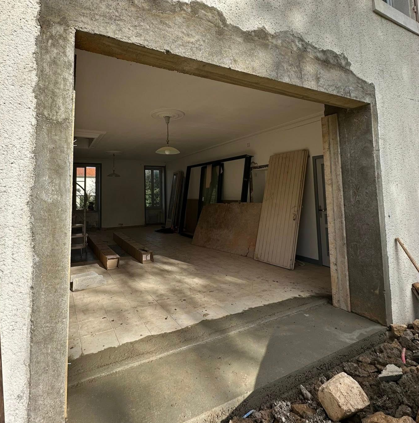 Vue extérieure d'une ouverture de bâtiment avec ossature apparente. Intérieur visible : pièce, matériaux et allée en béton.