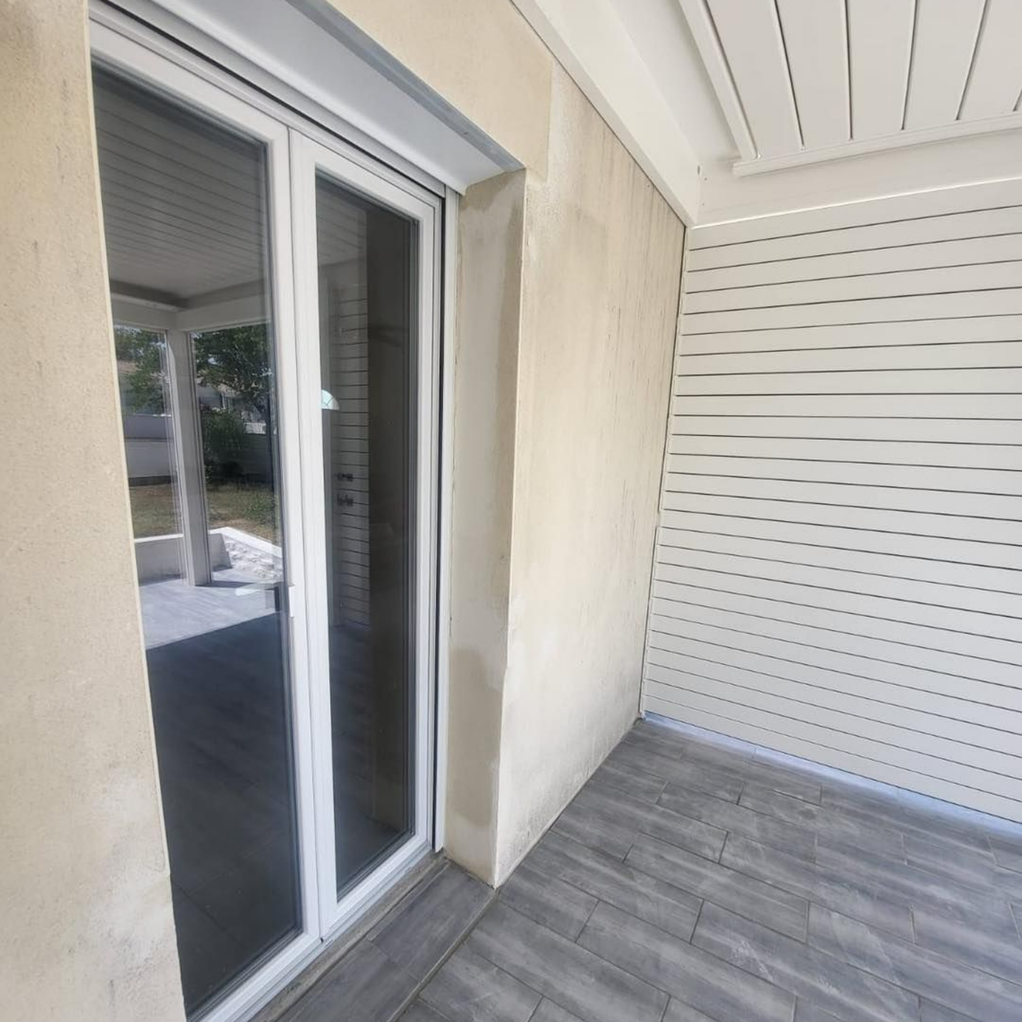 Porte-fenêtre et bardage blancs sur un bâtiment de couleur claire avec un sol gris.
