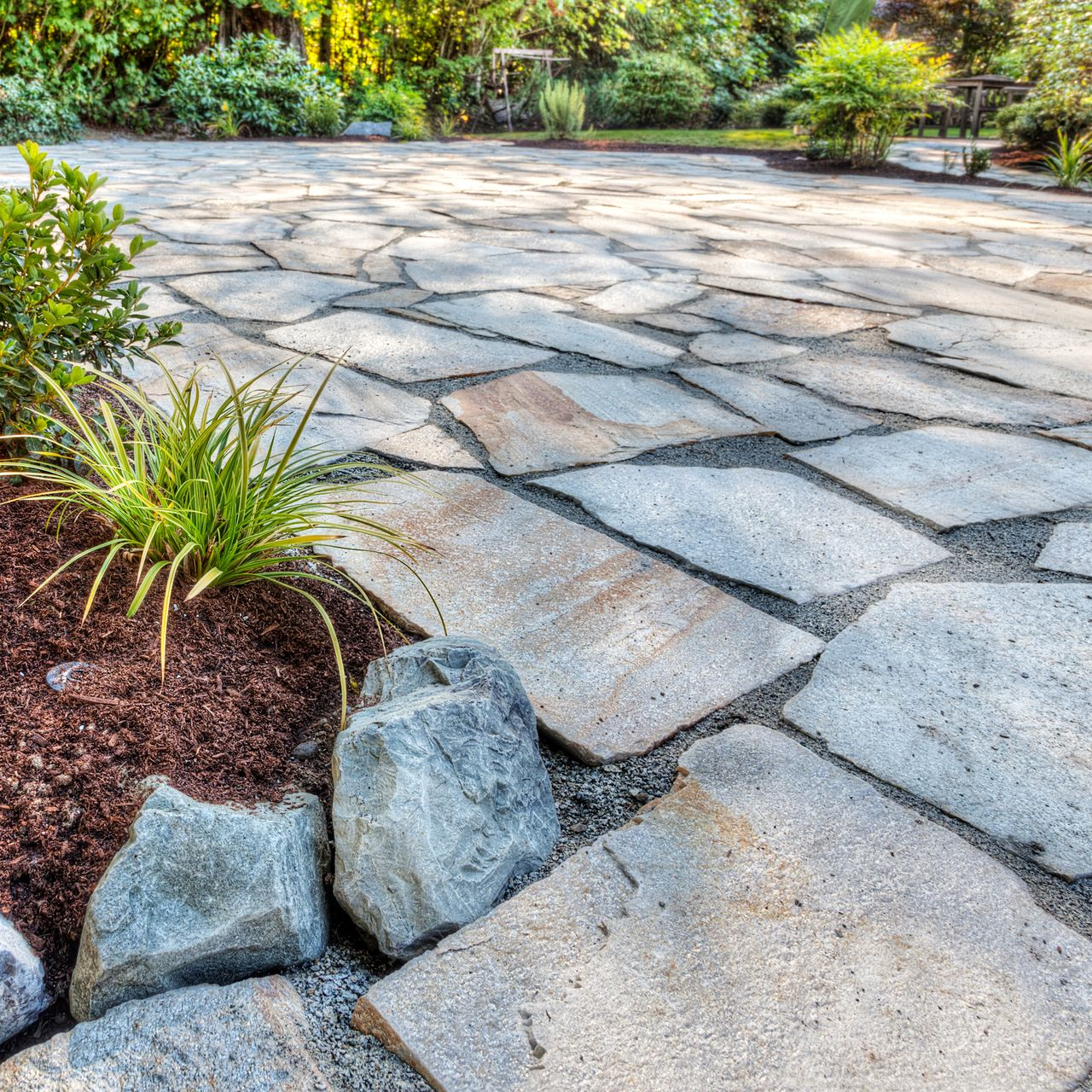 Terrasse en pierre avec dalles de forme irrégulière, entourée de plantes et de paillis.