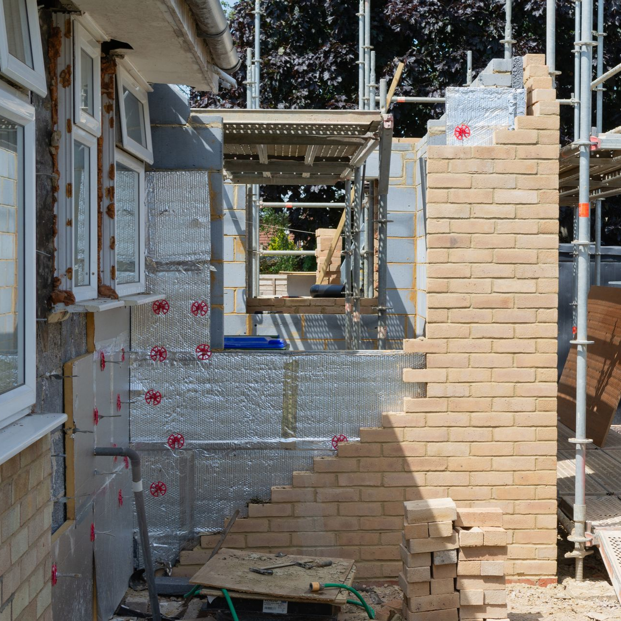Extérieur d'un bâtiment en construction, montrant la maçonnerie, l'isolation et les échafaudages.