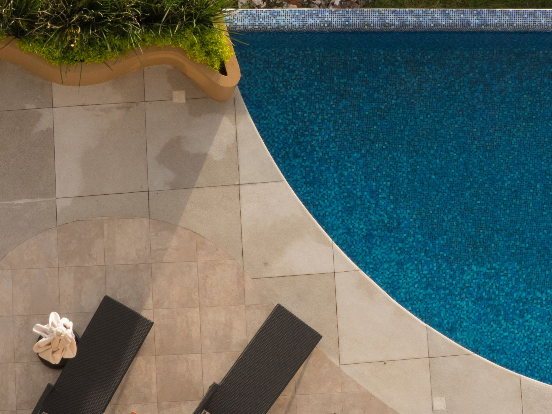 Vue aérienne de la piscine à l'eau bleu foncé, de la terrasse claire et de deux chaises longues noires.