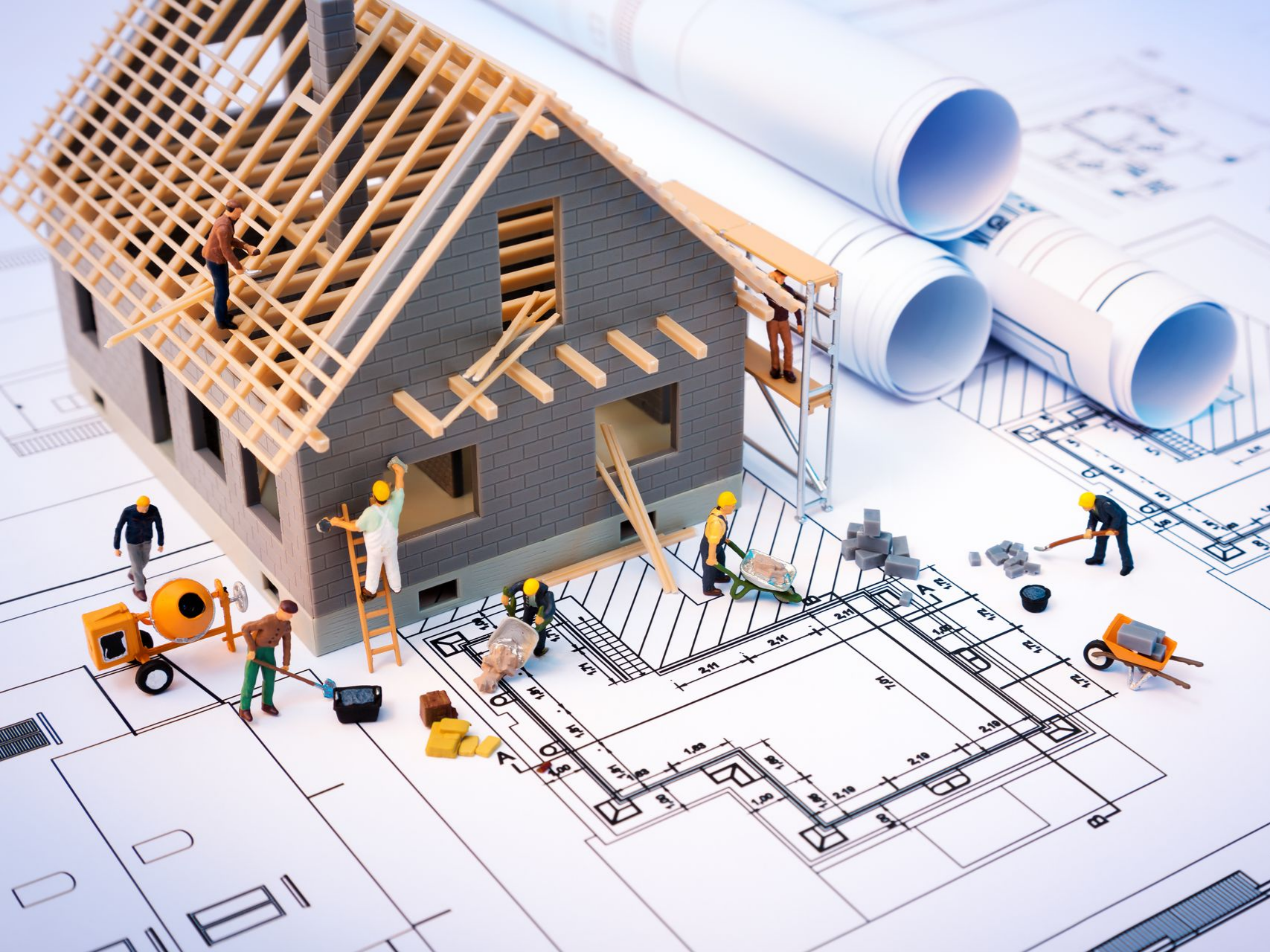 Maison miniature en construction avec plans, outils et ouvriers du bâtiment.