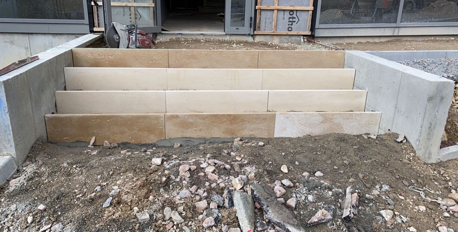 Des marches en pierre mènent à un bâtiment extérieur, construit en blocs de couleur claire, scellés dans du béton.