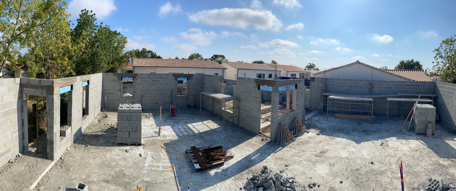 Chantier de construction en cours, avec des murs en parpaings de béton, sous un ciel bleu.