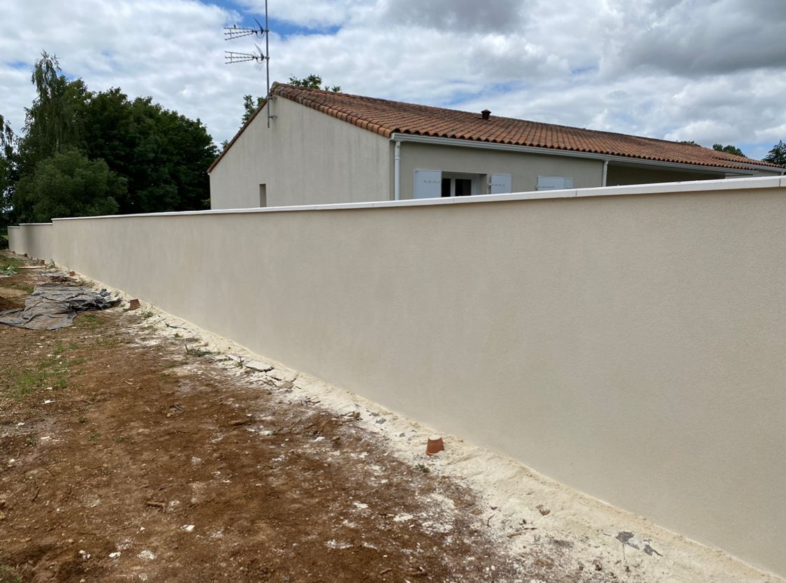 Mur en stuc beige avec une maison en arrière-plan par une journée ensoleillée.