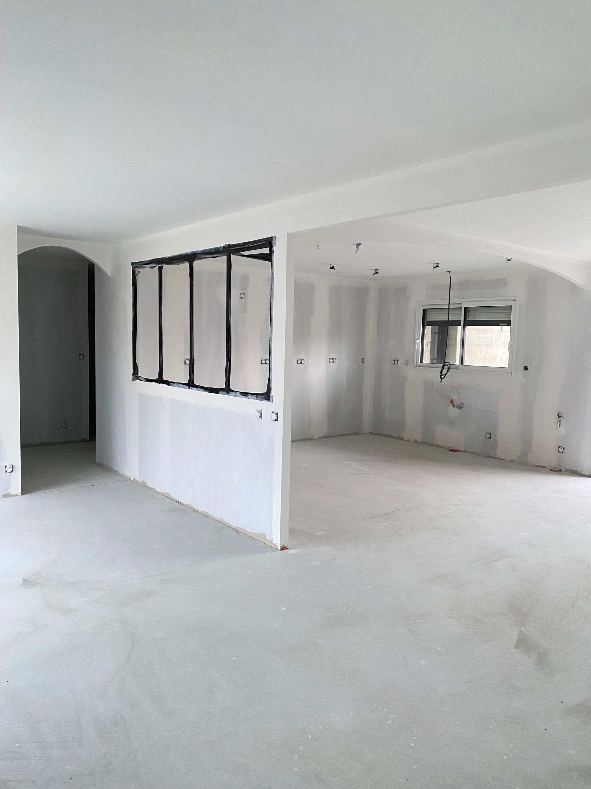 Intérieur d'une pièce neuve aux murs blancs, avec une fenêtre et un cadre en métal noir.