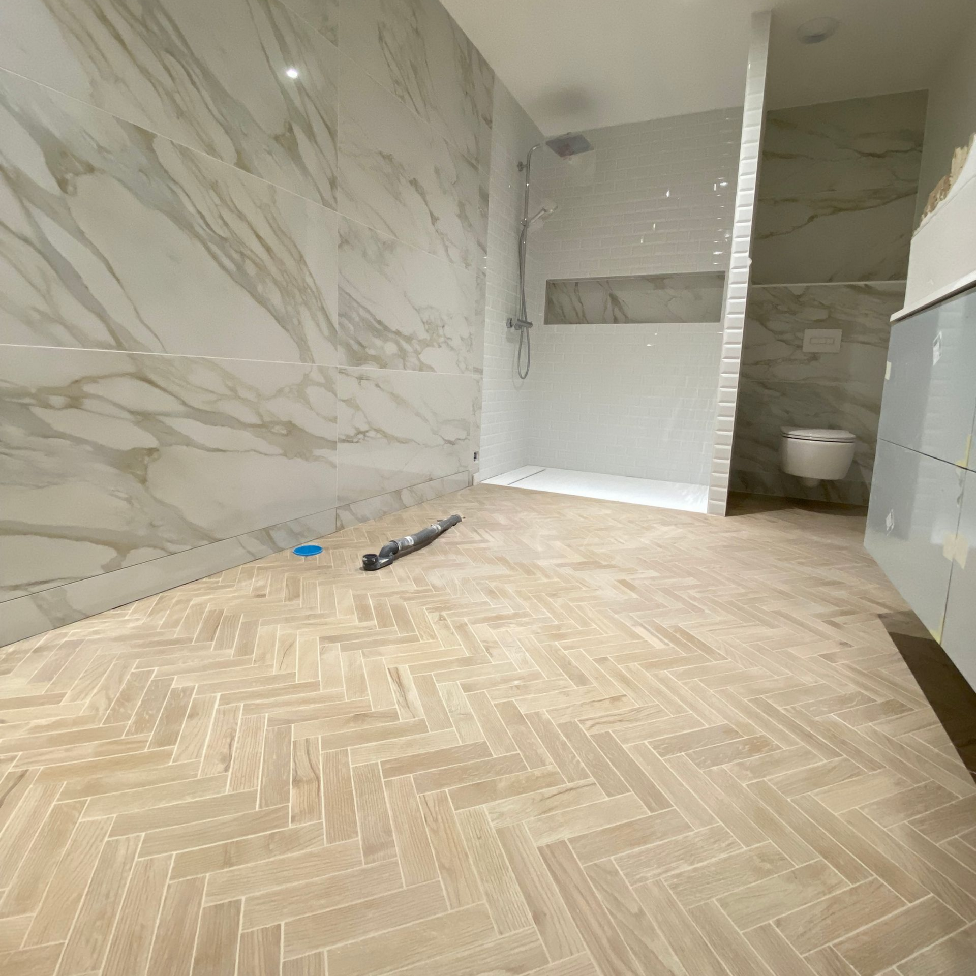 Salle de bains avec parquet clair à chevrons, murs en marbre et espace douche.