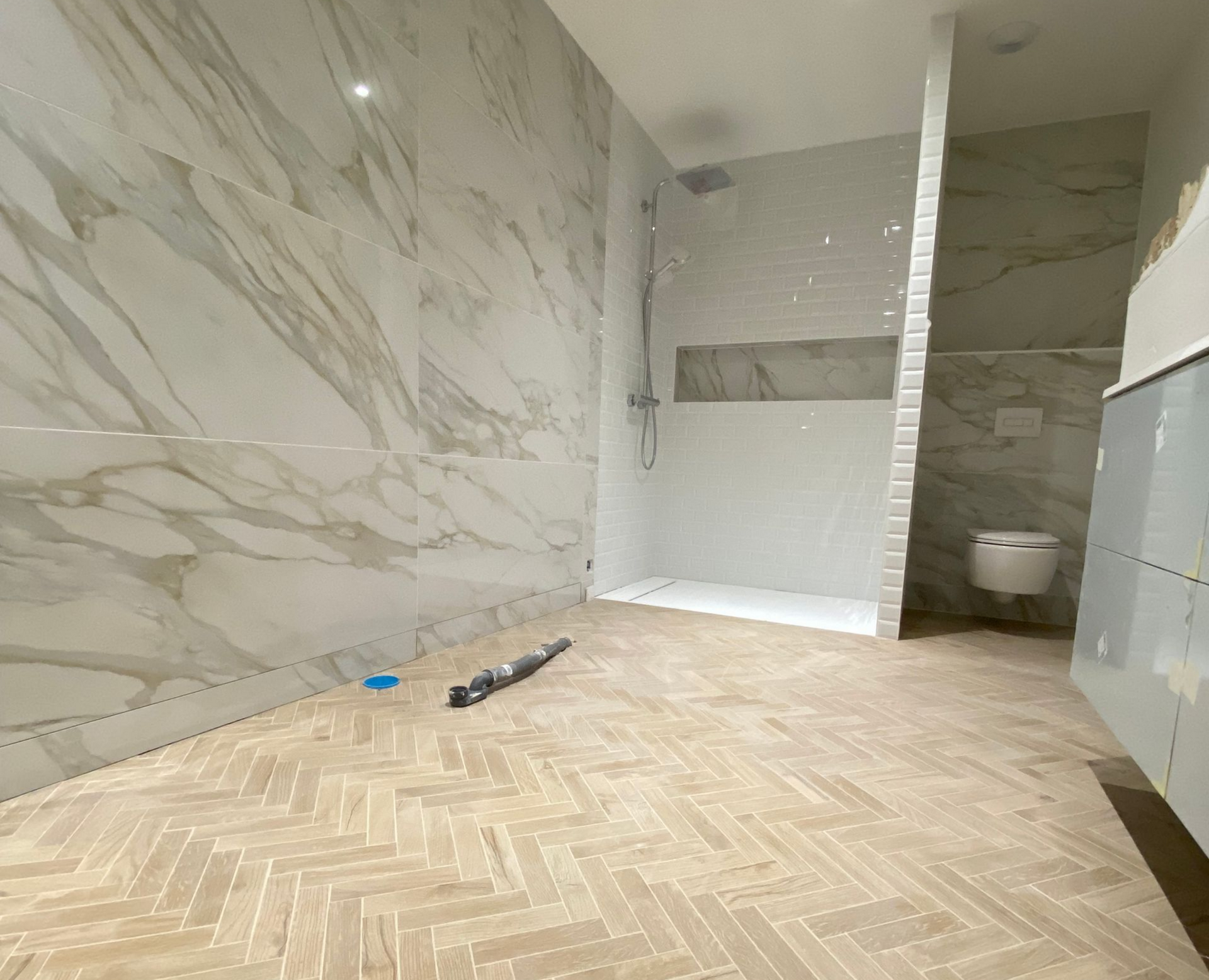 Salle de bains spacieuse avec murs carrelés en marbre, sol à chevrons, douche à l'italienne et toilettes.