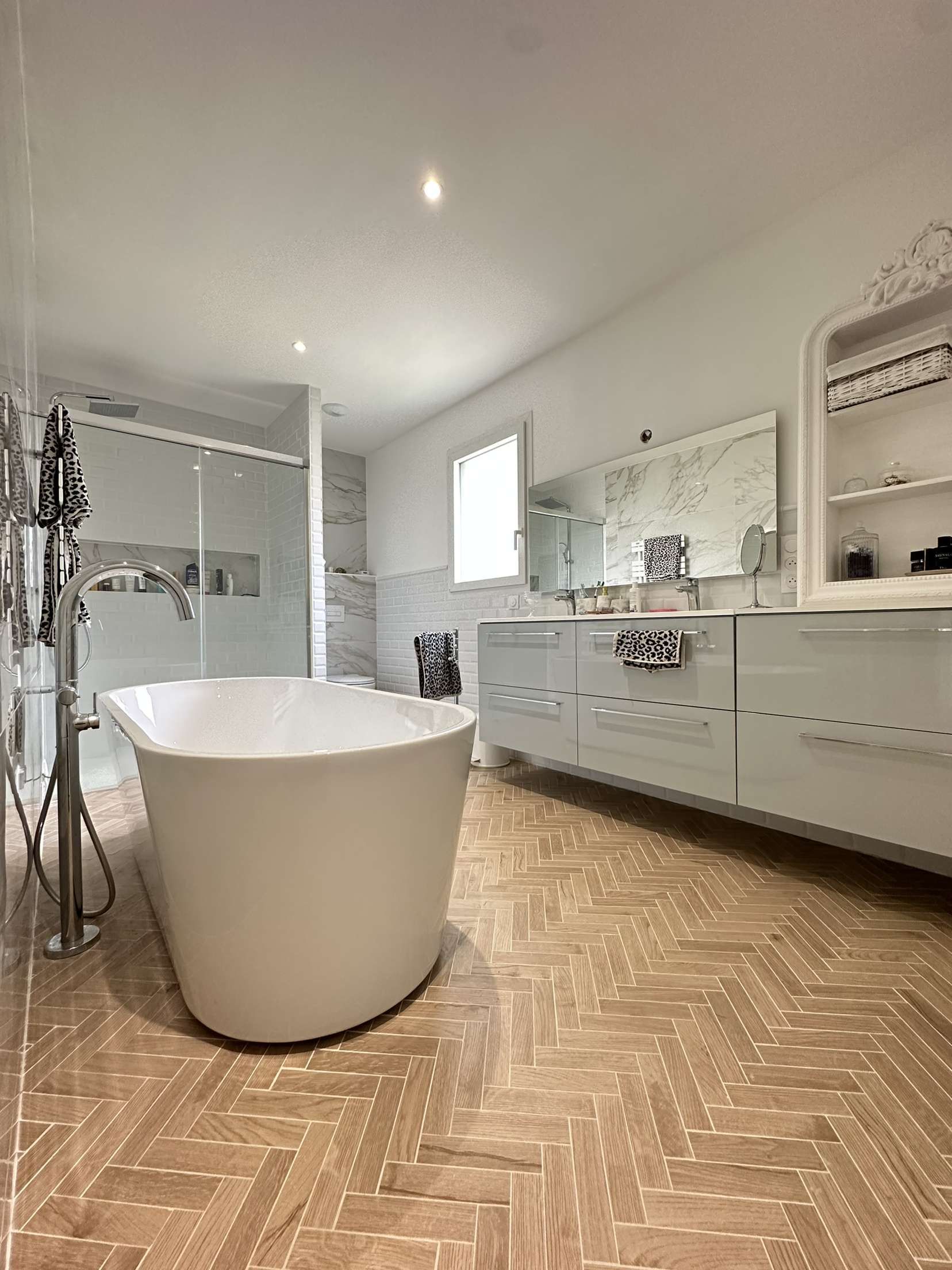 Salle de bains élégante avec baignoire îlot, grande vasque et parquet à chevrons.