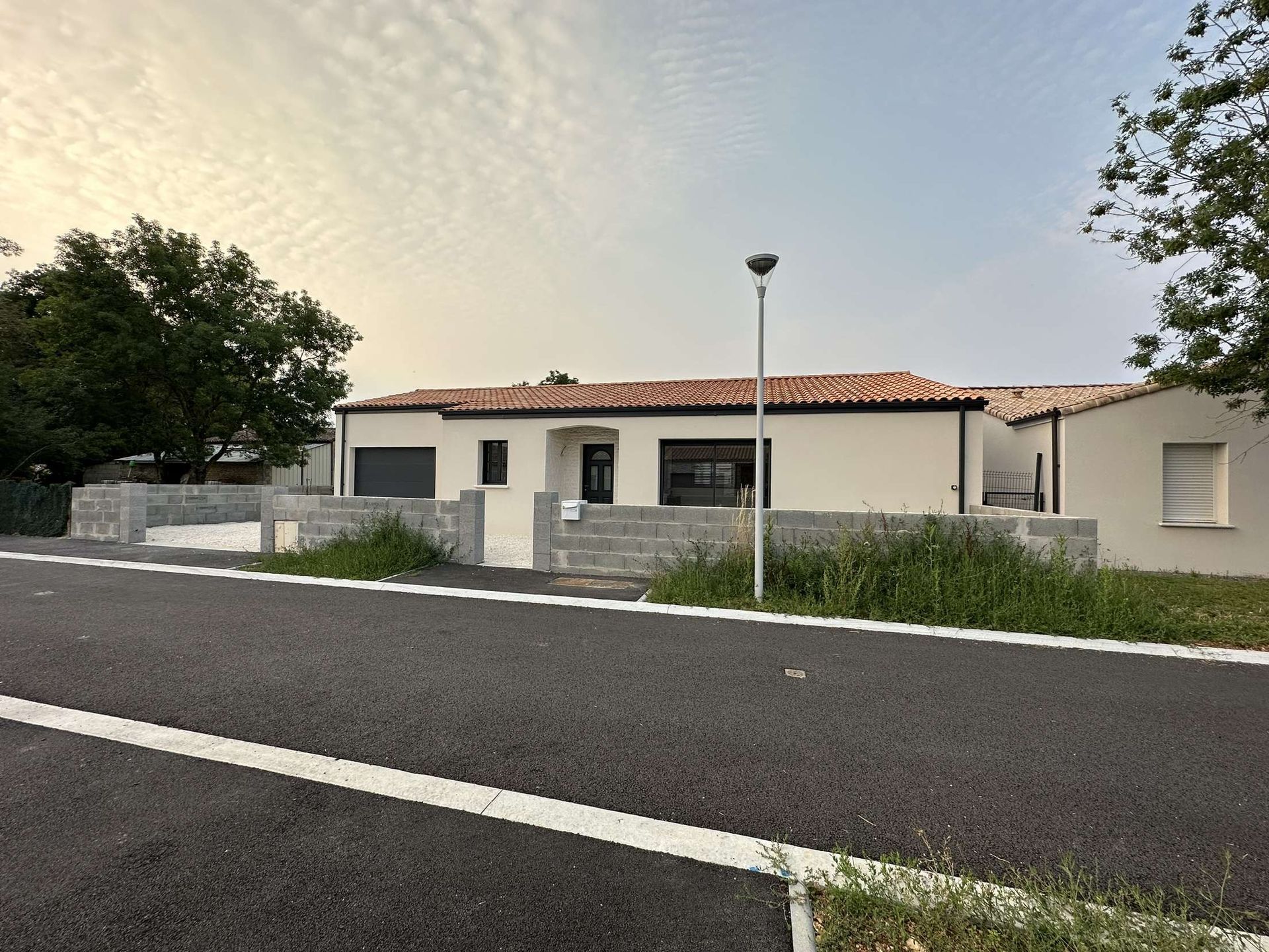 Maison blanche avec des boiseries noires, un toit de tuiles rouges et un mur de pierre grise en façade.