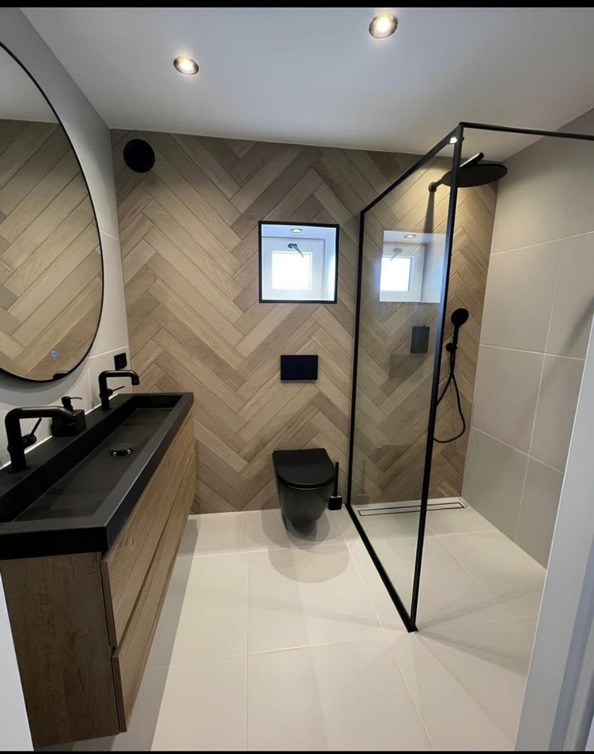 Salle de bains moderne avec mur d'accent en bois à chevrons, robinetterie noire et douche en verre.