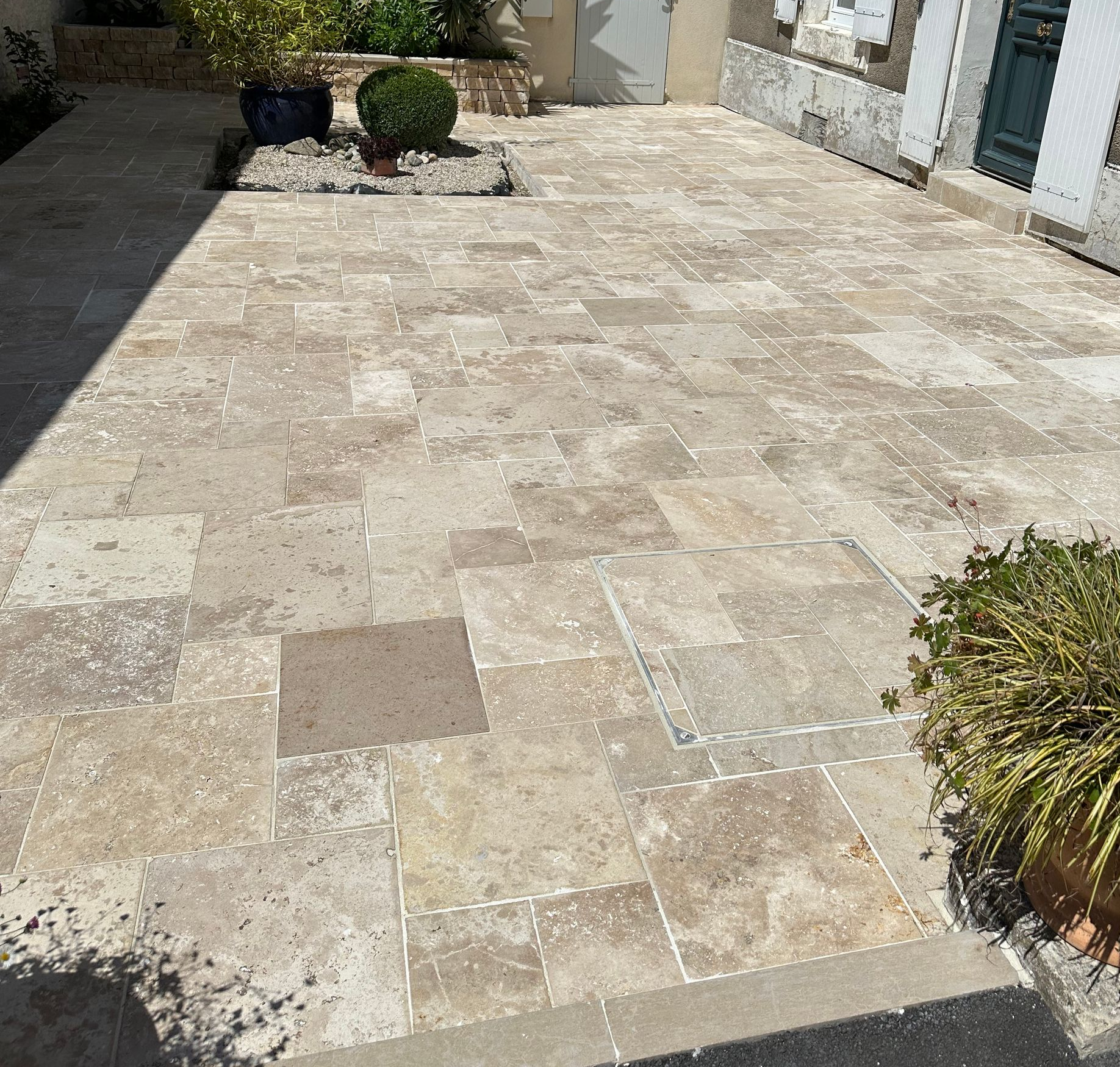 Terrasse en pierre avec plantes en pot et entrée du bâtiment.