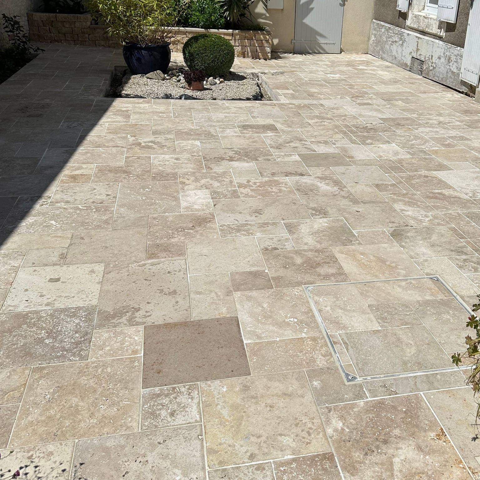 Mur en pierre bordant une piscine, avec de la verdure au-dessus et des arbres en arrière-plan.