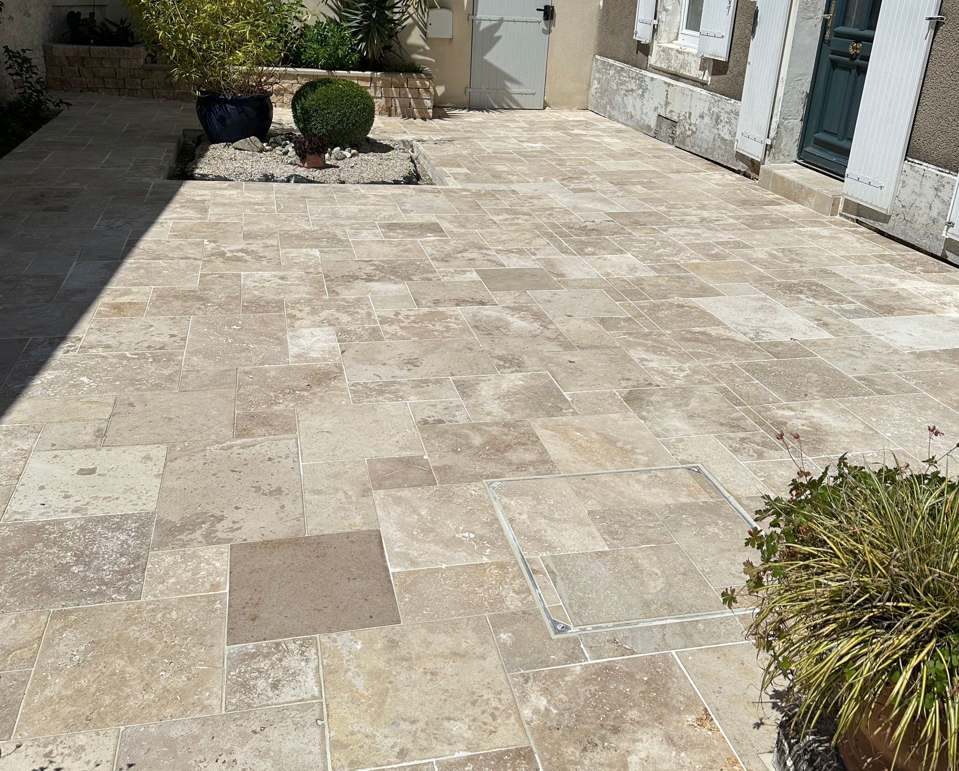 Terrasse en pierre grise avec jardinière intégrée et marches. La terrasse est entourée de gazon.