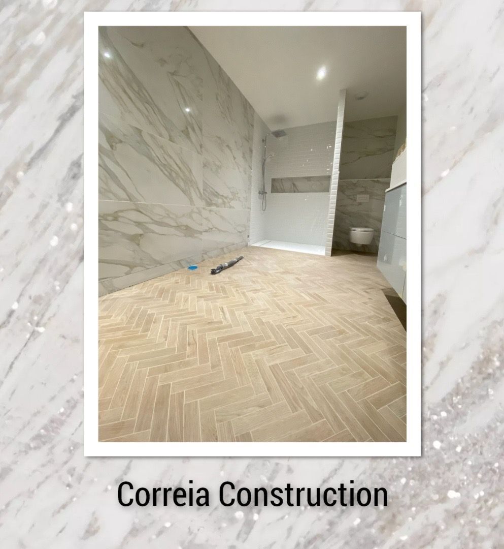 Salle de bains avec parquet à chevrons et murs carrelés imitation marbre. Logo de Correia Construction.