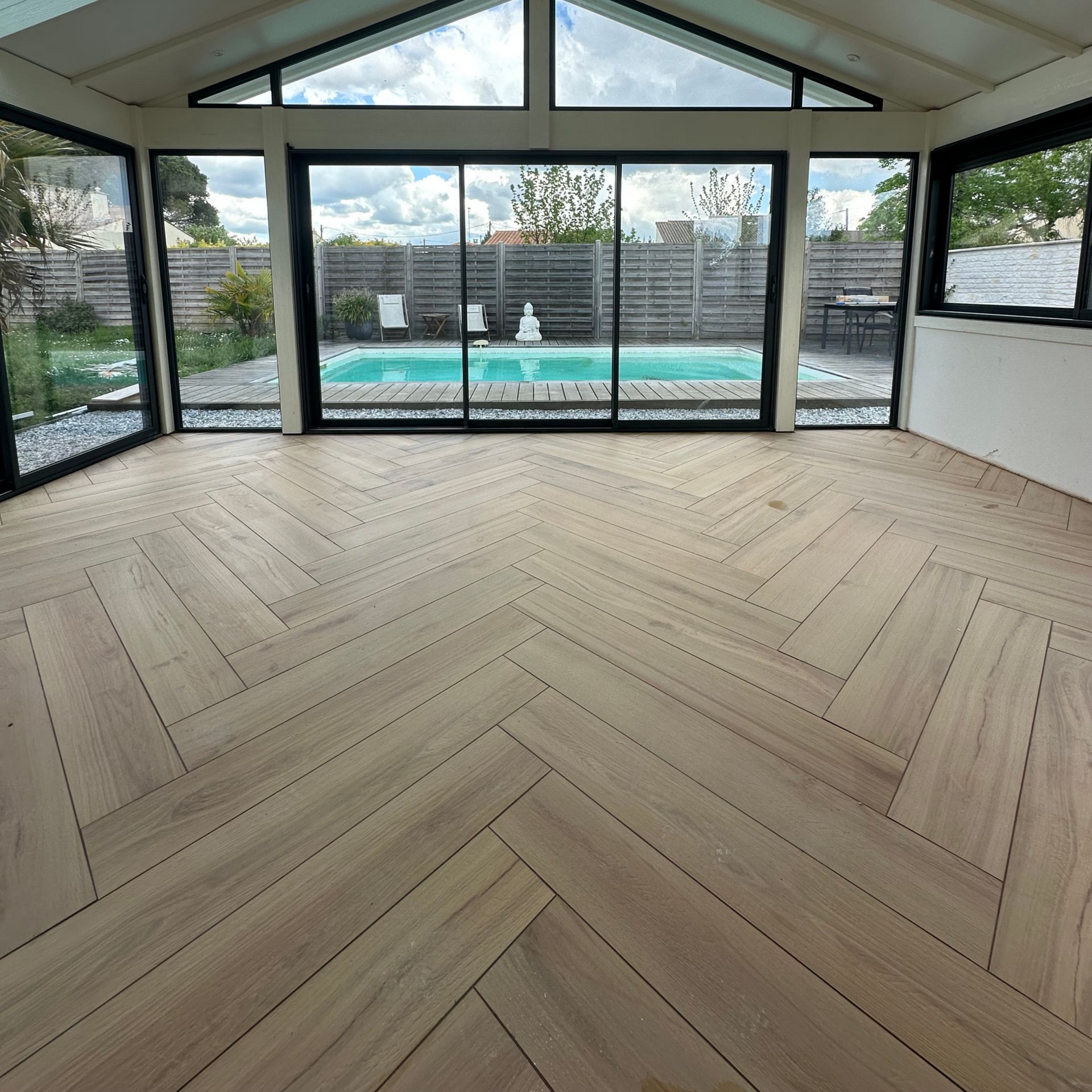 Véranda avec parquet à chevrons donnant sur une piscine et un jardin, et dotée de grandes fenêtres.