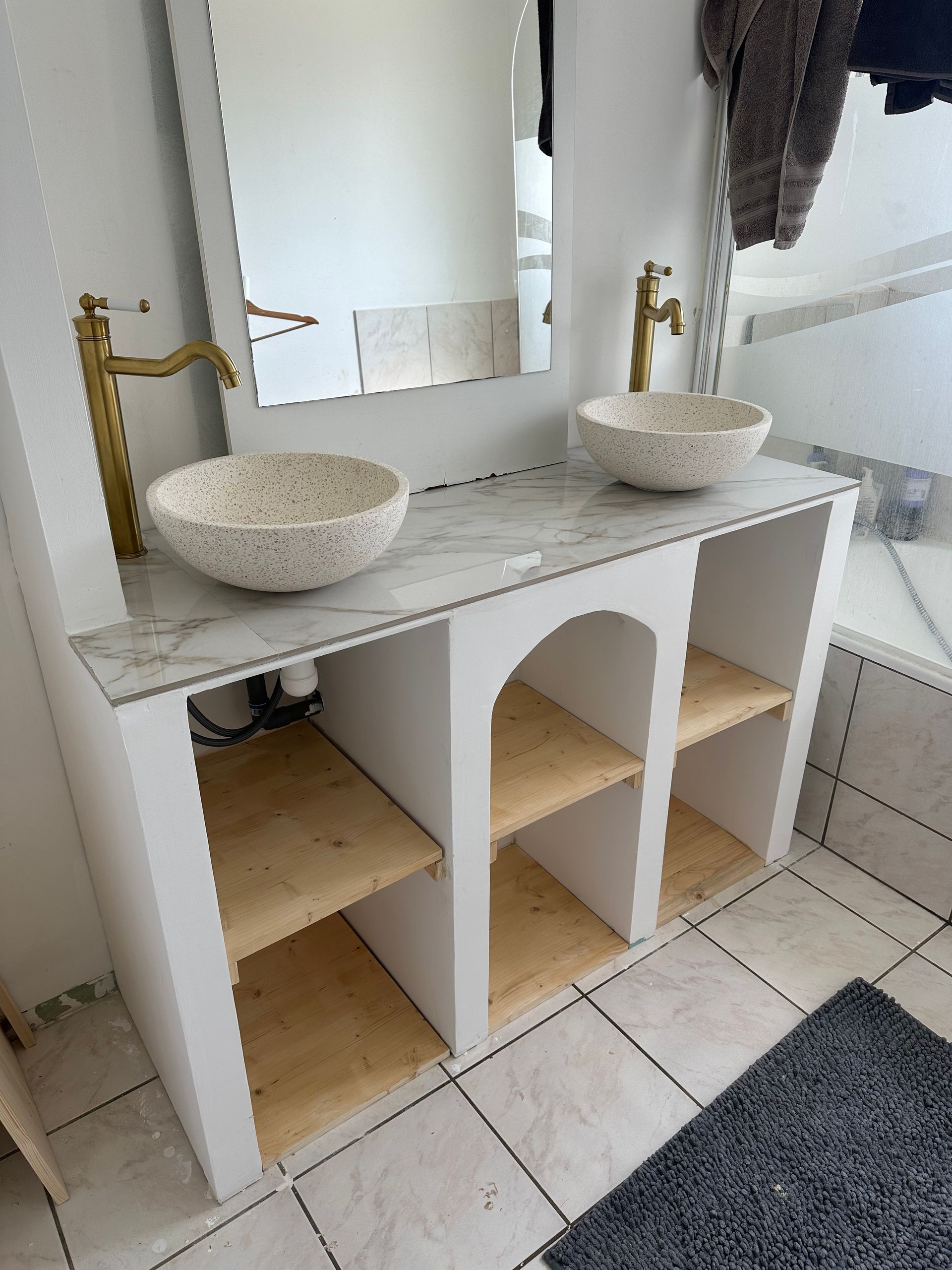 Meuble-lavabo blanc avec plateau en marbre, deux vasques mouchetées et robinetterie dorée.