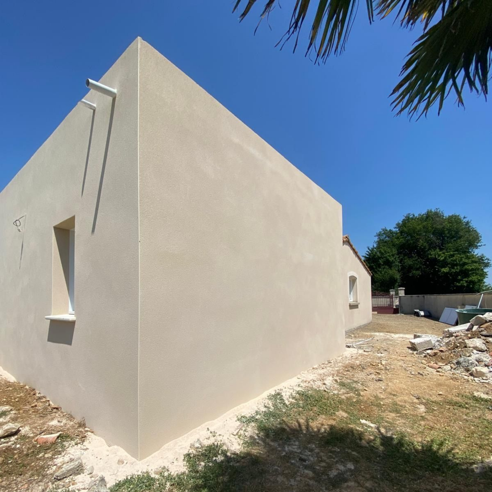Vue extérieure d'une maison beige nouvellement construite sous un ciel bleu clair, aménagement paysager inachevé.
