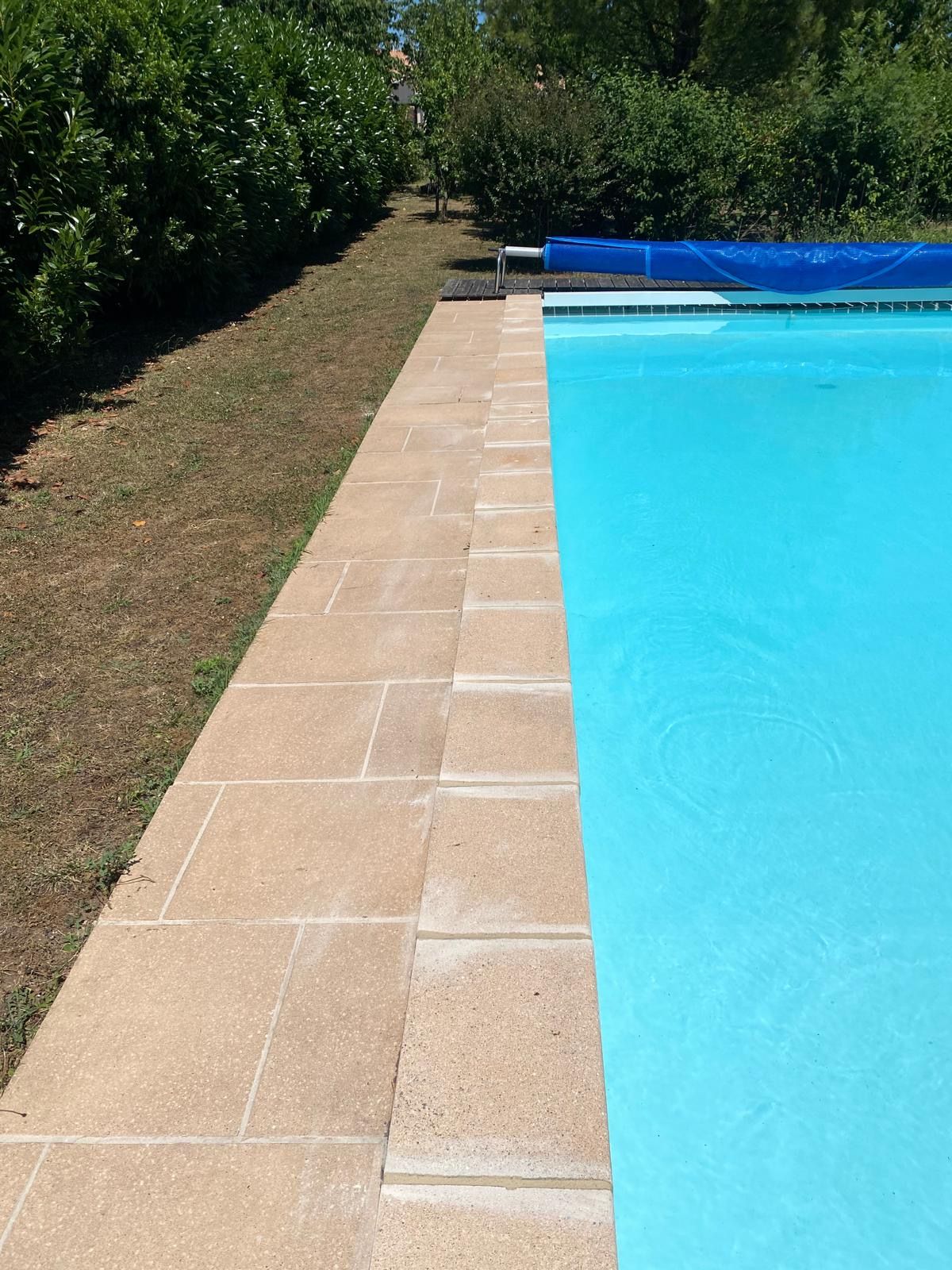 Vue depuis le bord d'une piscine à l'eau bleue et aux carreaux de pierre.