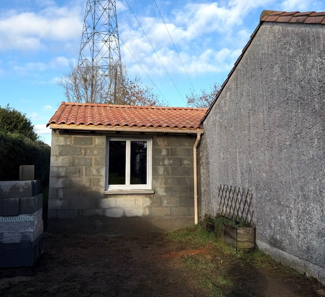 Extérieur d'une maison neuve aux murs en stuc beige clair, se détachant sur un ciel bleu éclatant.