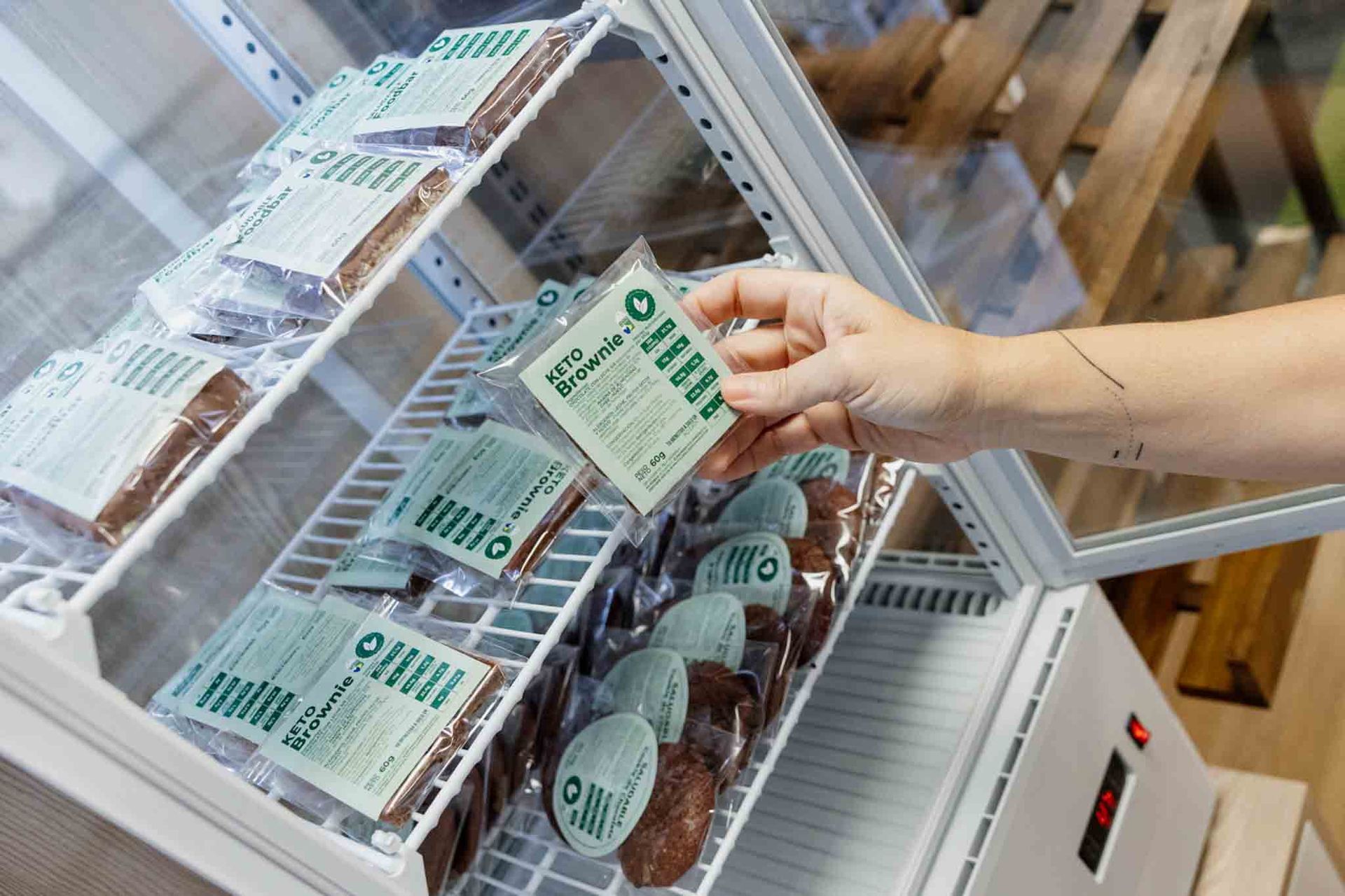 Una mano sostiene un producto envasado de una nevera portátil. Los productos están perfectamente apilados en su interior.