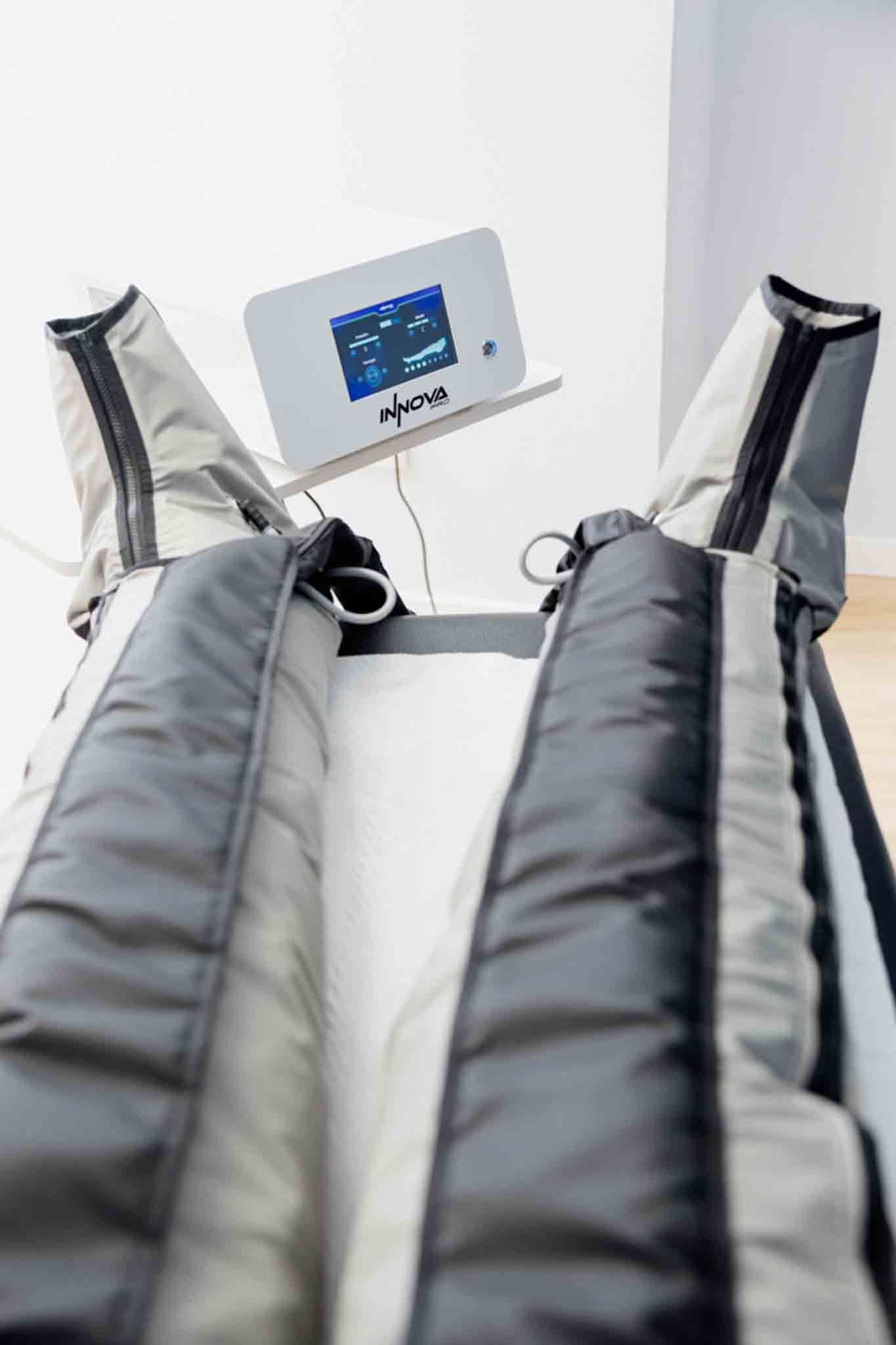 Dispositivo de terapia de compresión de piernas con mangas grises y negras y un panel de control conectado.