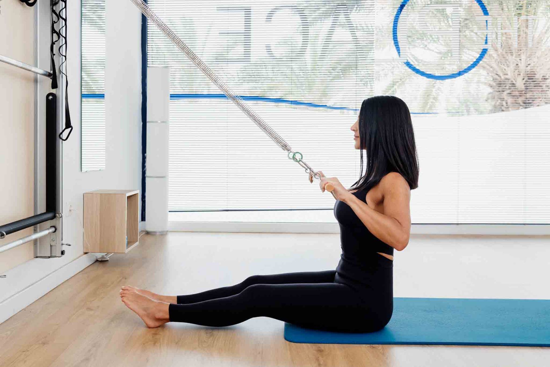 Una mujer practica pilates con remo en un estudio, tirando de una cuerda sujeta a un aparato.