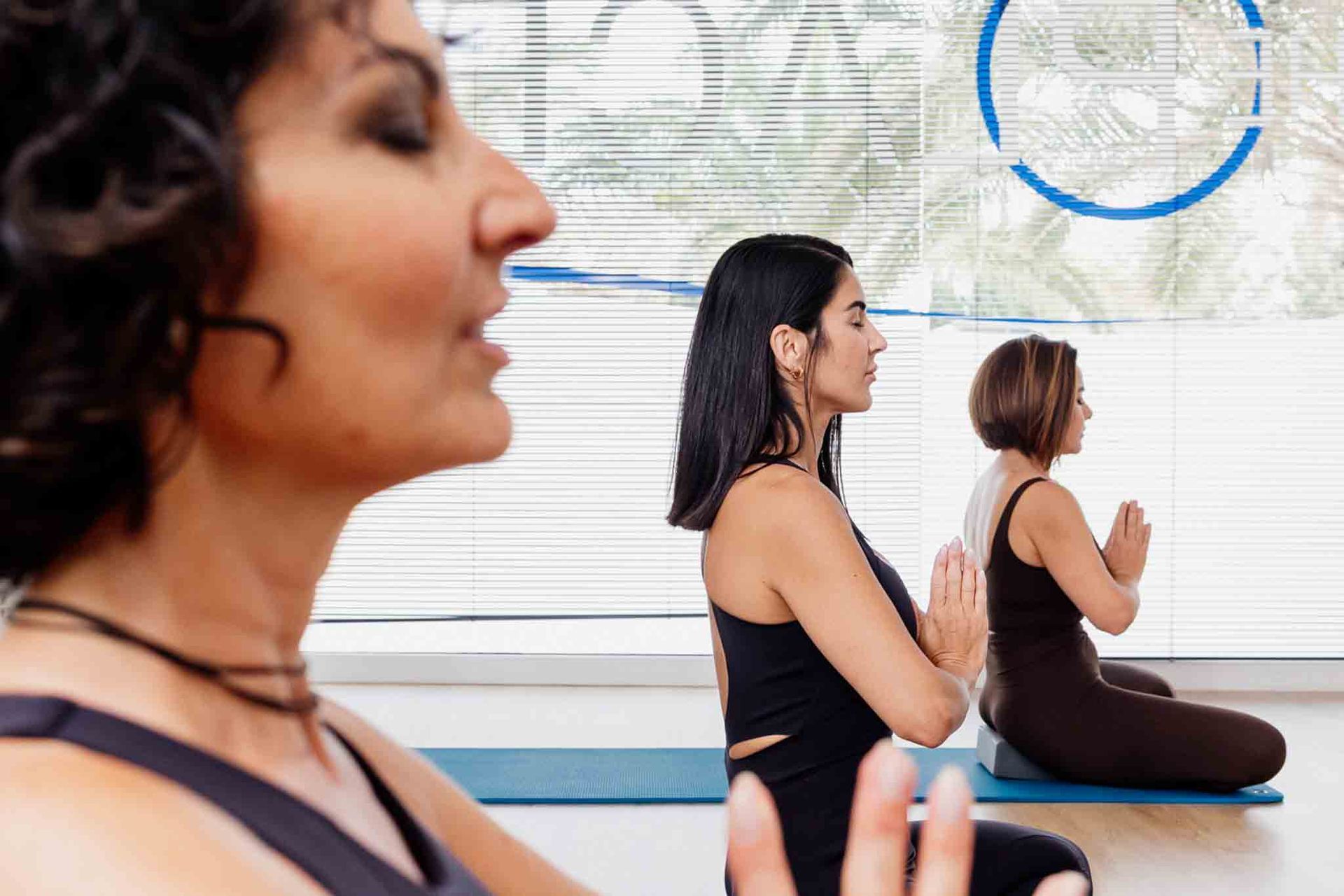 Mujeres en una clase de yoga, meditando con los ojos cerrados y las manos en posición de oración.