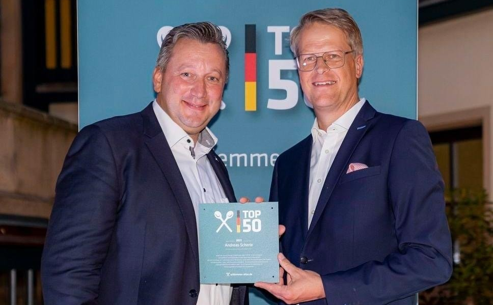 Zwei Männer in Anzügen halten ein Schild mit der Aufschrift „Top 50“