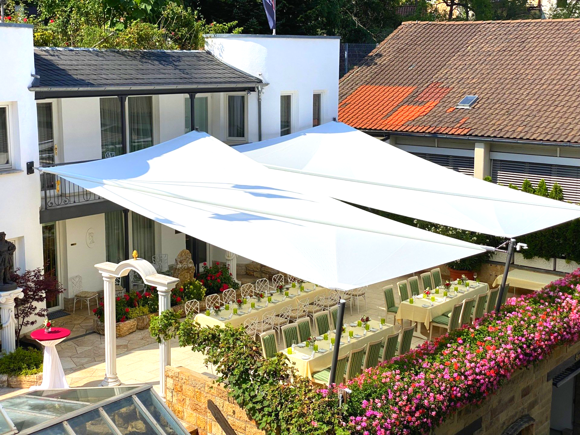 Ein großer weißer Sonnenschirm überdacht eine Terrasse mit Tischen und Stühlen