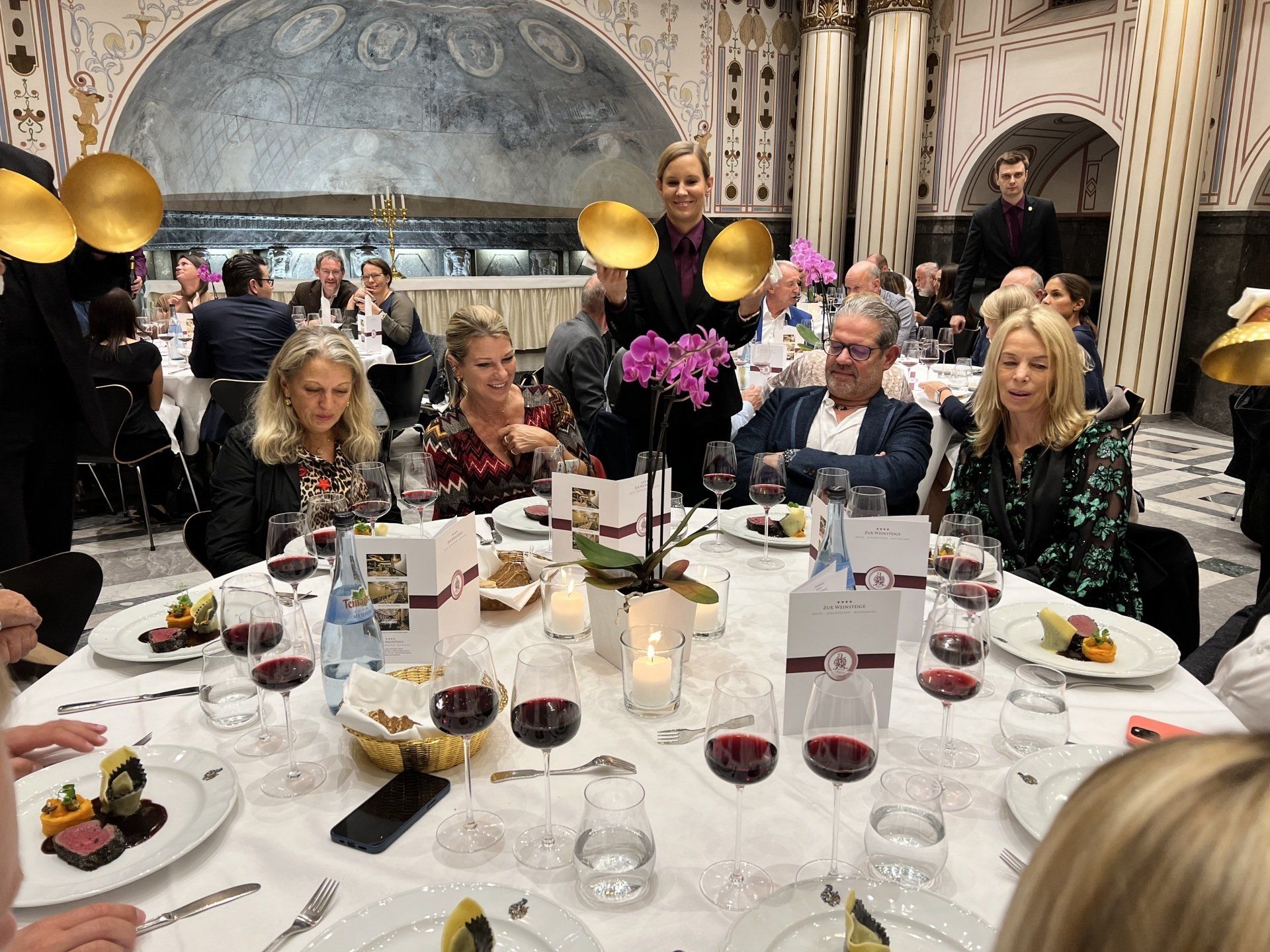 Eine Gruppe von Menschen sitzt an einem Tisch mit Tellern voller Essen und Weingläsern