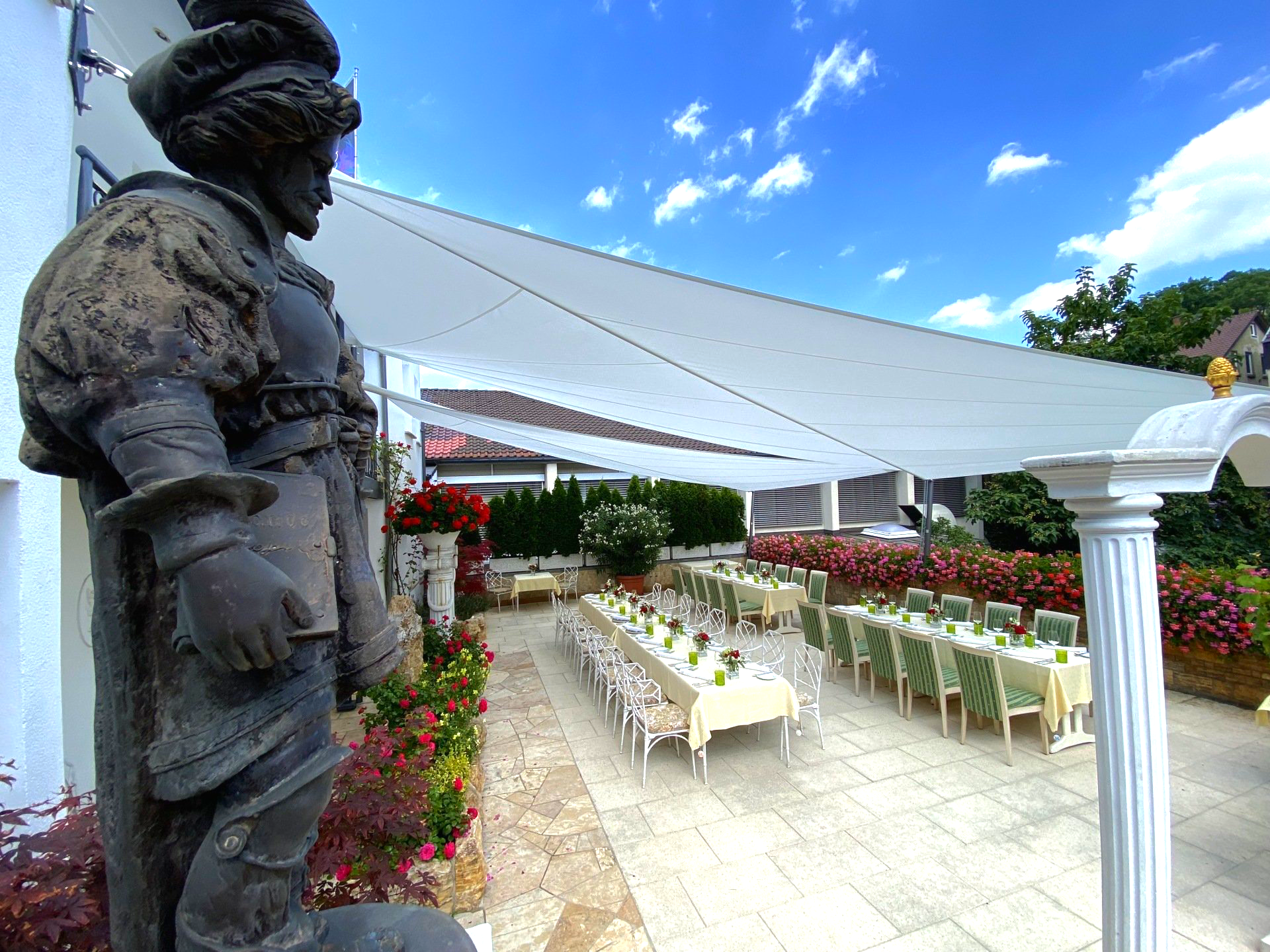 Eine Statue eines Mannes steht vor einer Terrasse mit Tischen und Stühlen
