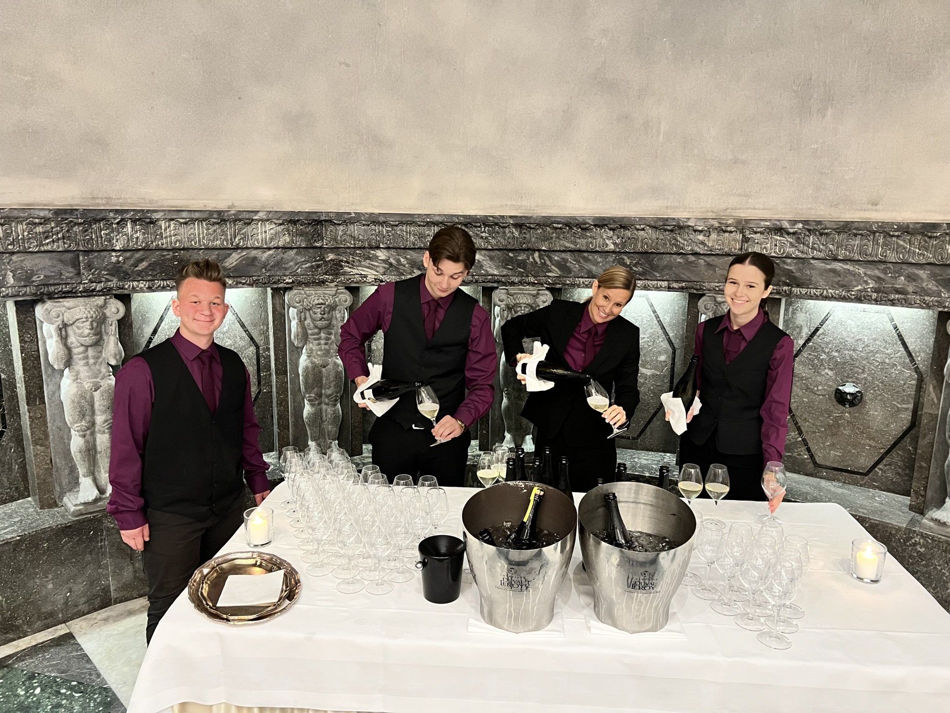 Eine Gruppe von Menschen steht mit Eimern Champagner um einen Tisch herum